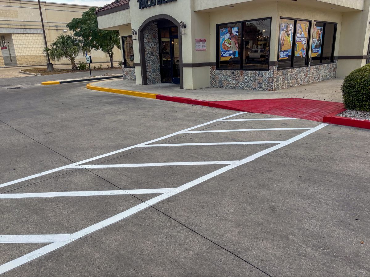 Fresh crosswalk markings with red fire lane curb at a commercial storefront