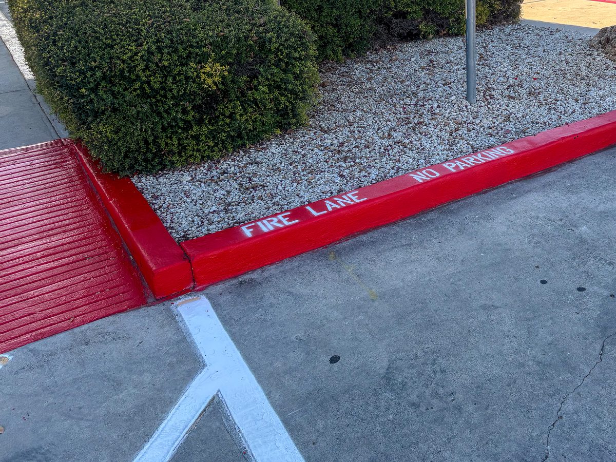Red fire lane curb painting with NO PARKING stencil at a commercial property