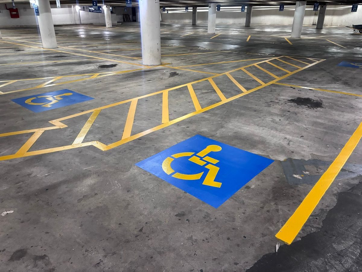 Freshly painted blue accessible stall symbols and yellow crosshatched access aisle in a parking garage