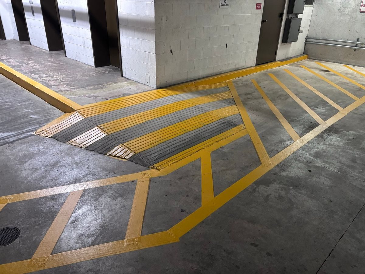 Yellow crosshatched walkway painted on a parking garage floor near a ramp