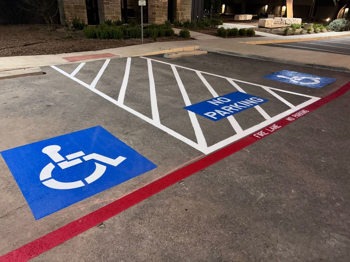 New accessible stall with blue symbol, crosshatched access aisle with NO PARKING, and red fire lane curb