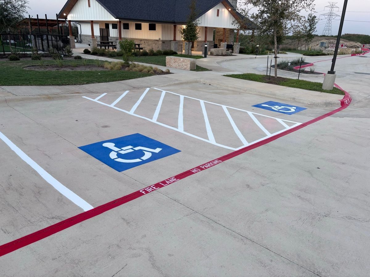 New accessible stall with blue symbol and crosshatched access aisle beside a red fire lane on fresh concrete
